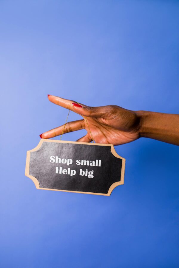 A hand holding a sign reading 'Shop small, Help big' against a blue background.